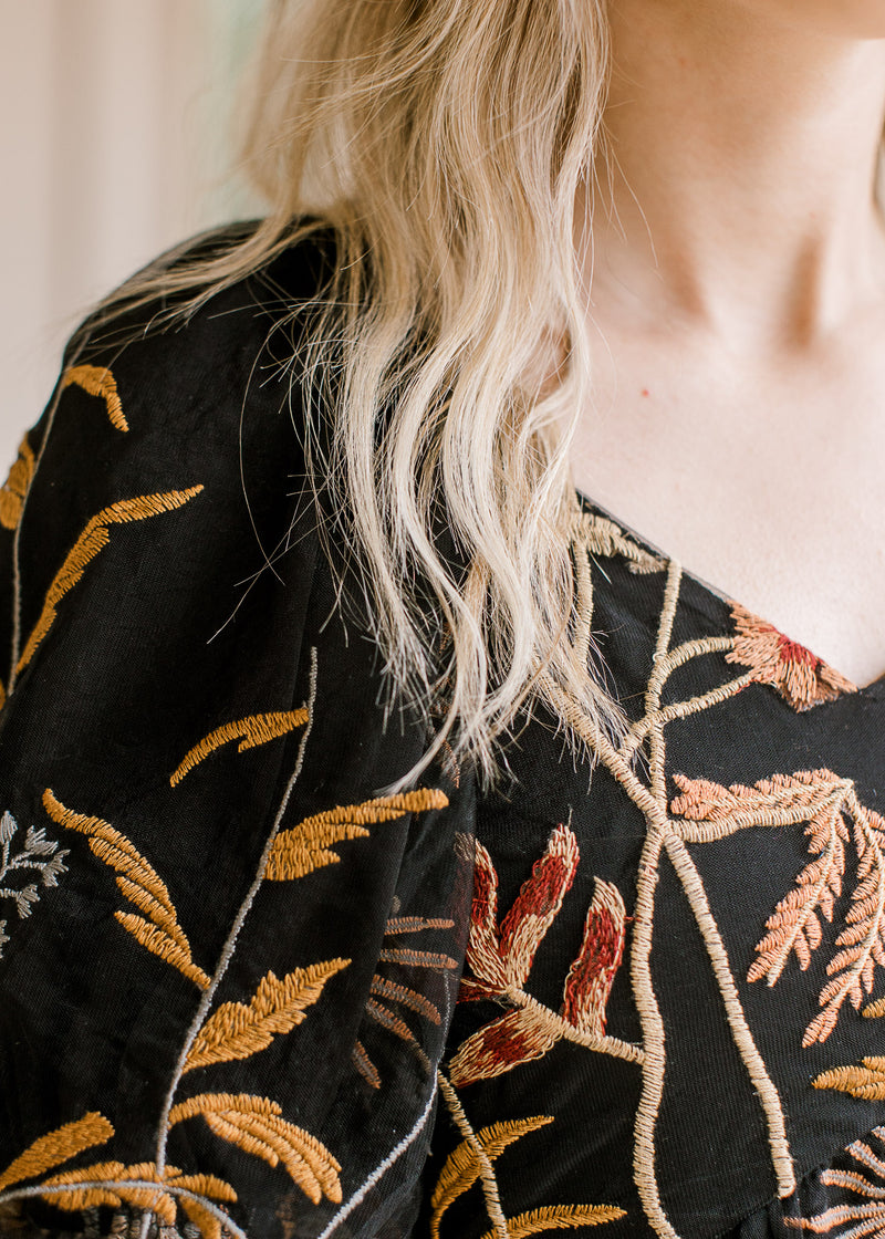 Close up of stitched golden browns, silver and maroon flowers on a black v-neck dress.