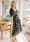 Model wearing a black dress with golden browns, silver and maroon flowers and bubble sleeves. 