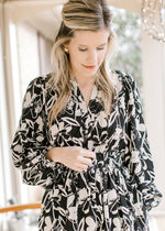 Close up of v-neck and smocked waist on a black midi with white flowers and long bubble sleeves.