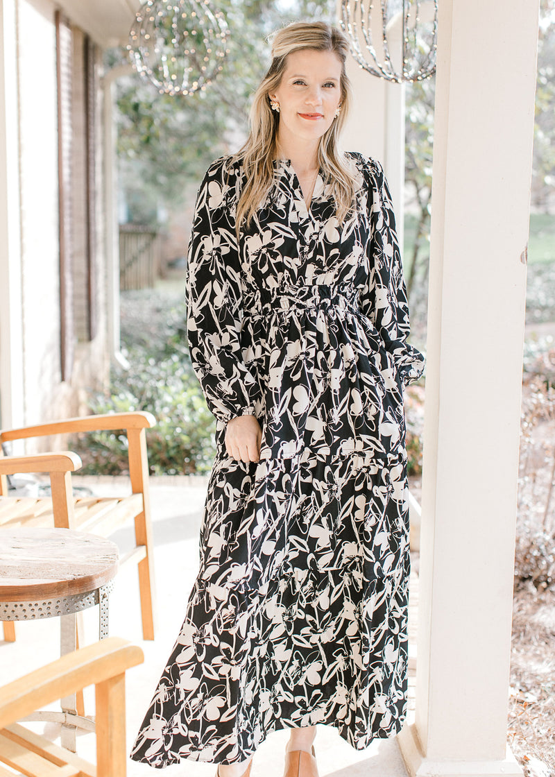 Model wearing mules and a black dress with white flowers, smocked waist and long sleeves.