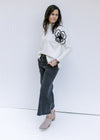 Model wearing a cream sweater with black embroidered flower detail, mock neckline and long sleeves.