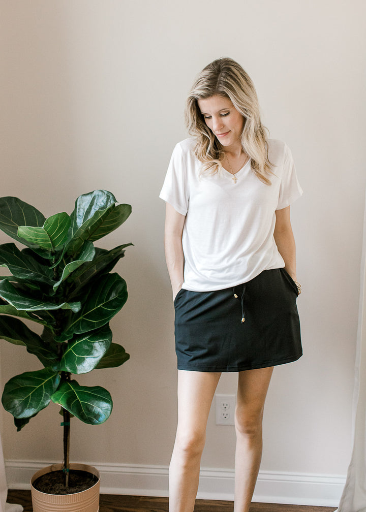 Model wearing a black skort with a white v-neck top with short sleeves and a lightweight fabric.