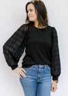 Model with hand on hip wearing a black top with a round neck and lace bubble long sleeves. 