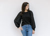 Model wearing jeans with a black top with a round neck and lace bubble long sleeves. 