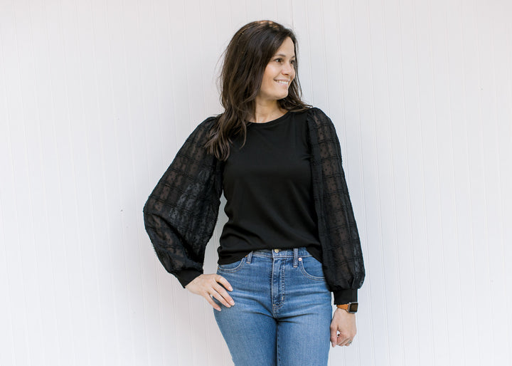 Model wearing jeans with a black top with a round neck and lace bubble long sleeves. 