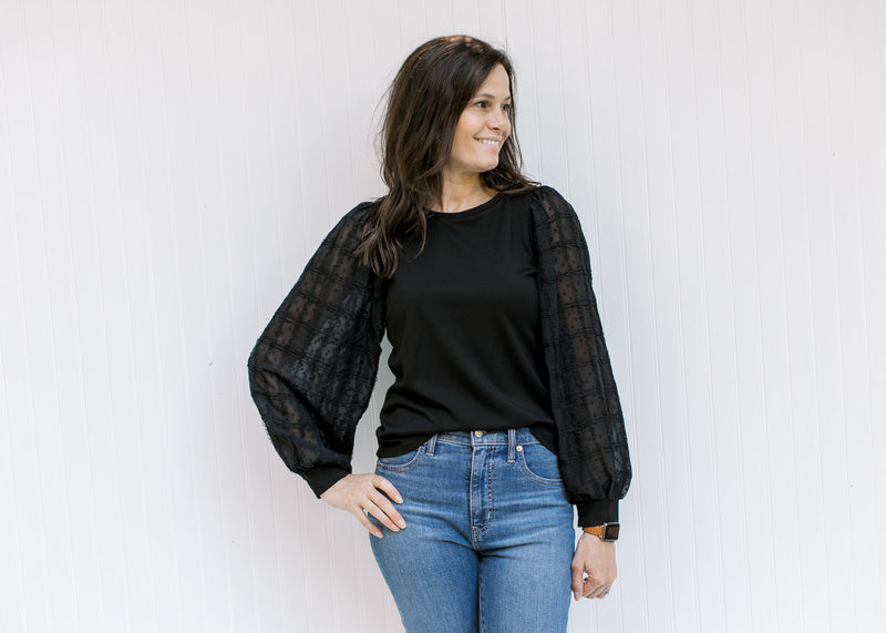 Model wearing jeans with a black top with a round neck and lace bubble long sleeves. 