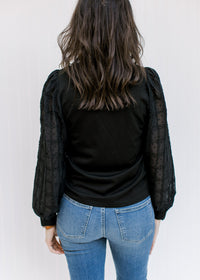 Back view of Model wearing a black top with a round neck and lace bubble long sleeves. 