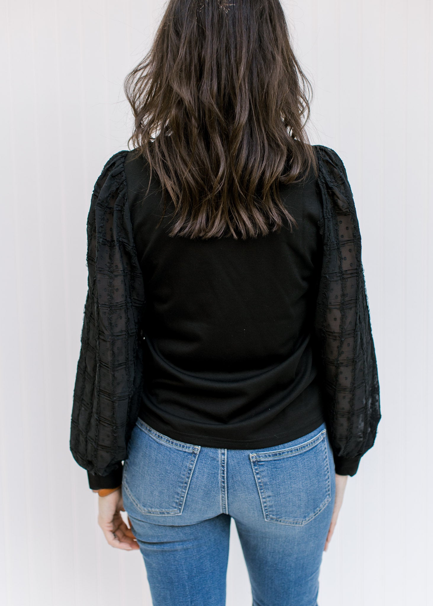 Back view of Model wearing a black top with a round neck and lace bubble long sleeves. 