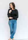 Model wearing blue jeans and a black top with a round neck and lace bubble long sleeves. 