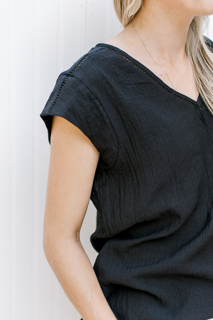 Close up of cap short sleeve and ladder trim on a black v-neck top.