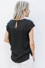 Back view of Model wearing a black top with ladder trim, v-neck, cap sleeves and keyhole closure.