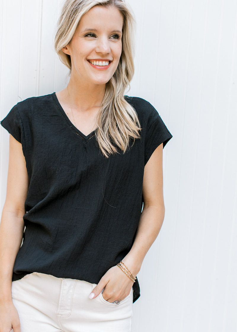 Model wearing a black top with ladder trim, v-neck and cap sleeves. 