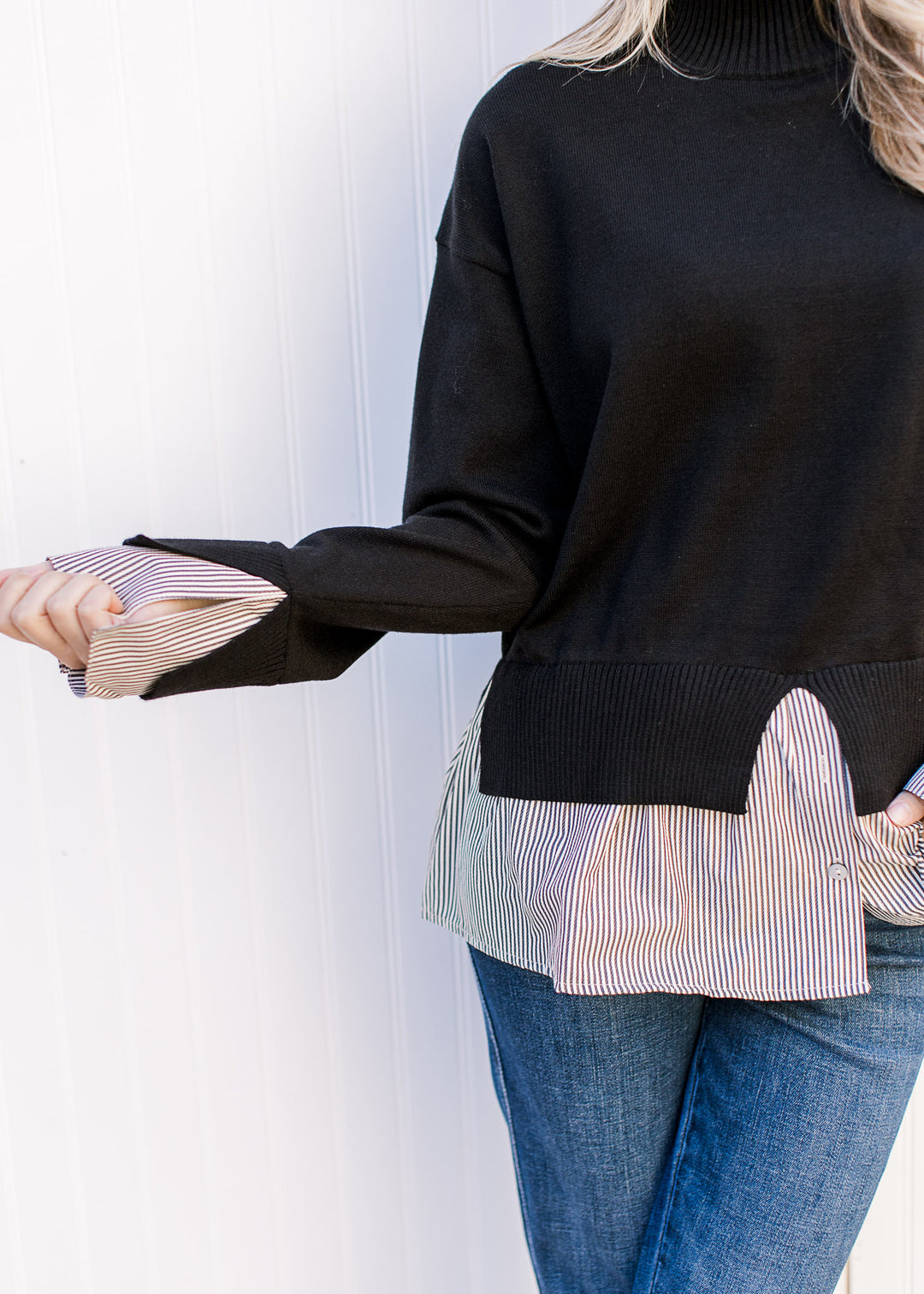 Close up of striped faux undershirt at cuff and hem of a black sweater with mock neck. 