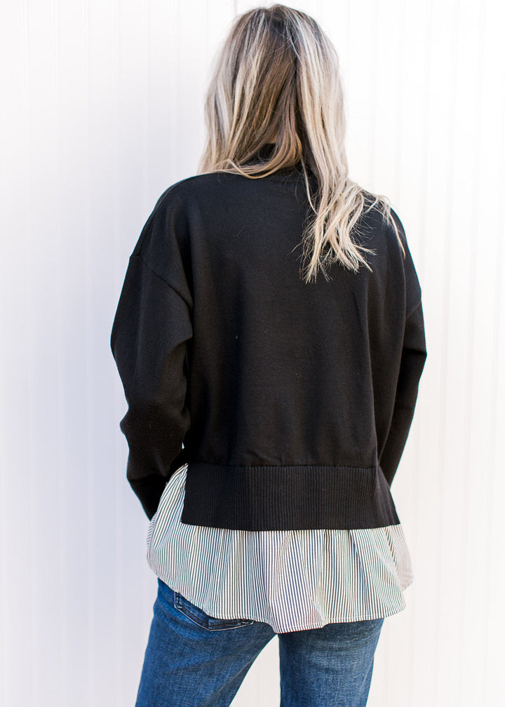 Back view of Model wearing a black sweater with attached black-and-white striped shirt. 