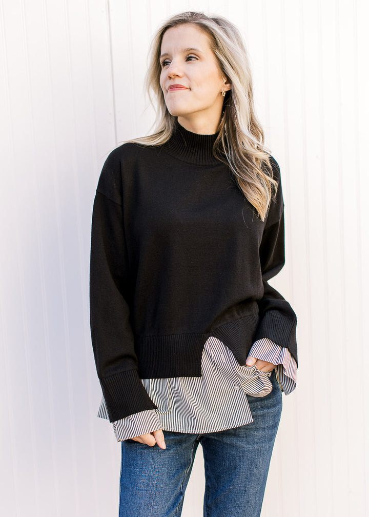 Model wearing jeans and a black sweater with attached black-and-white striped shirt with mock neck.