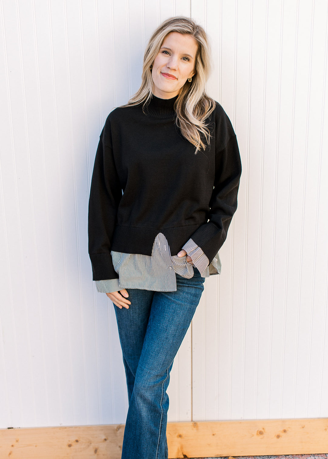 Model wearing a black sweater with attached black-and-white striped shirt and long sleeves. 