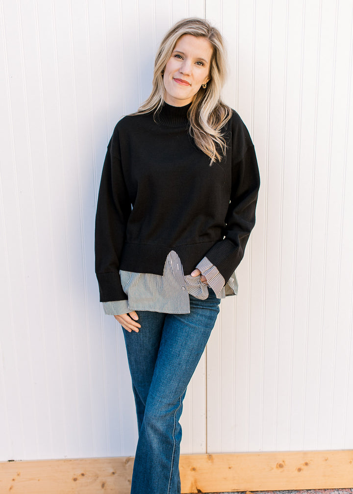 Model wearing a black sweater with attached black-and-white striped shirt and long sleeves. 