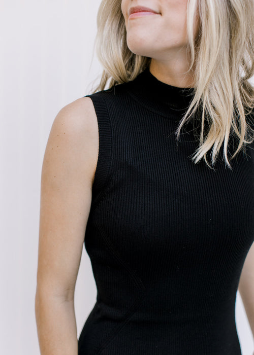 Close up view of model wearing a sleeveless black dress with a mock neck and a ribbed texture. 