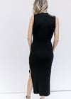 Back view of Model wearing a black sleeveless dress with a mock neckline and split side hem. 