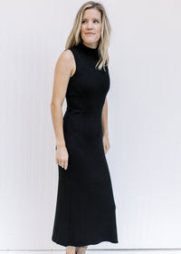 Model wearing a black sleeveless dress with a mock neckline, ribbed material and split side hem. 