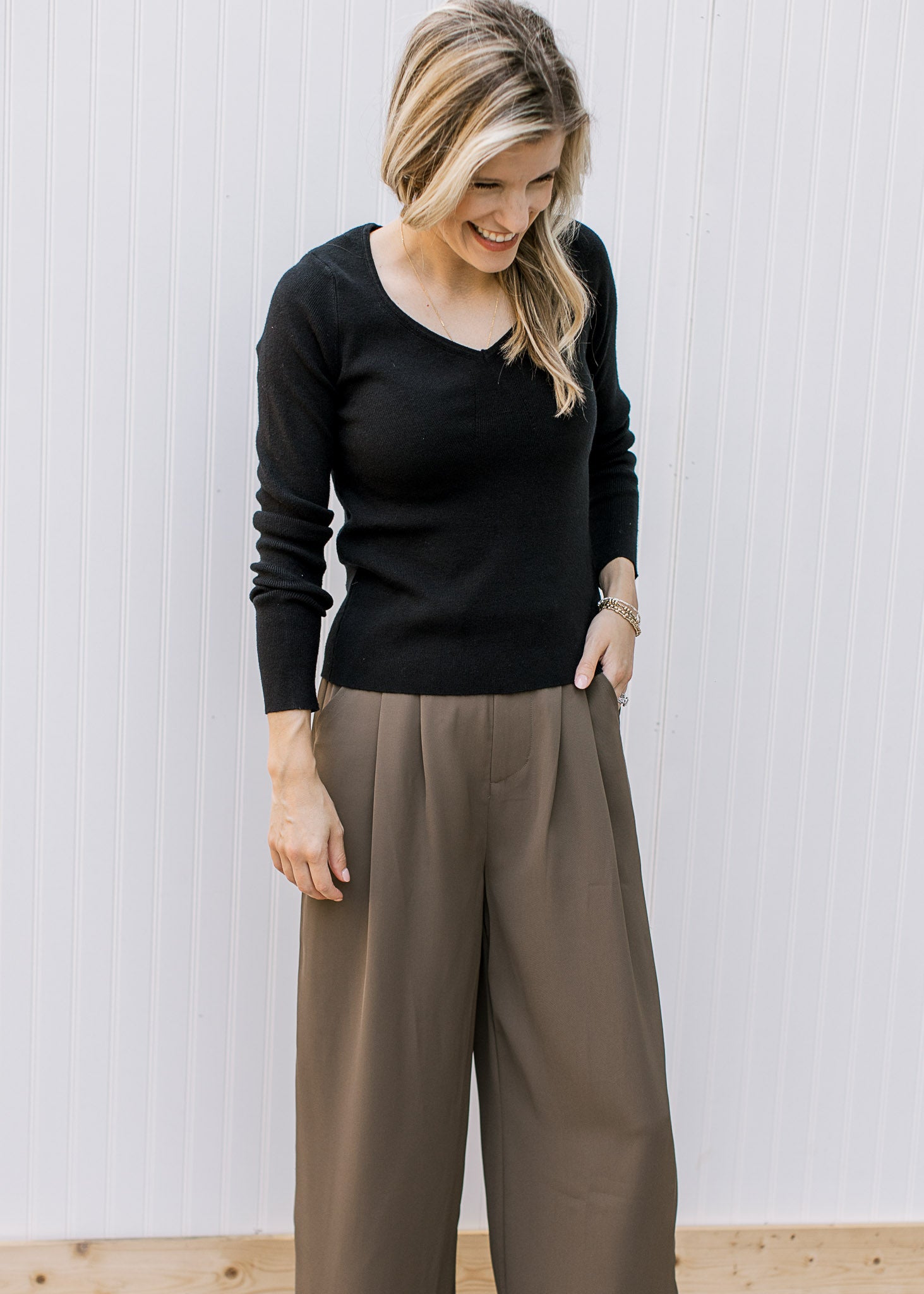 Model wearing brown pants with a black v-neck sweater with long sleeves and a ribbed material. 