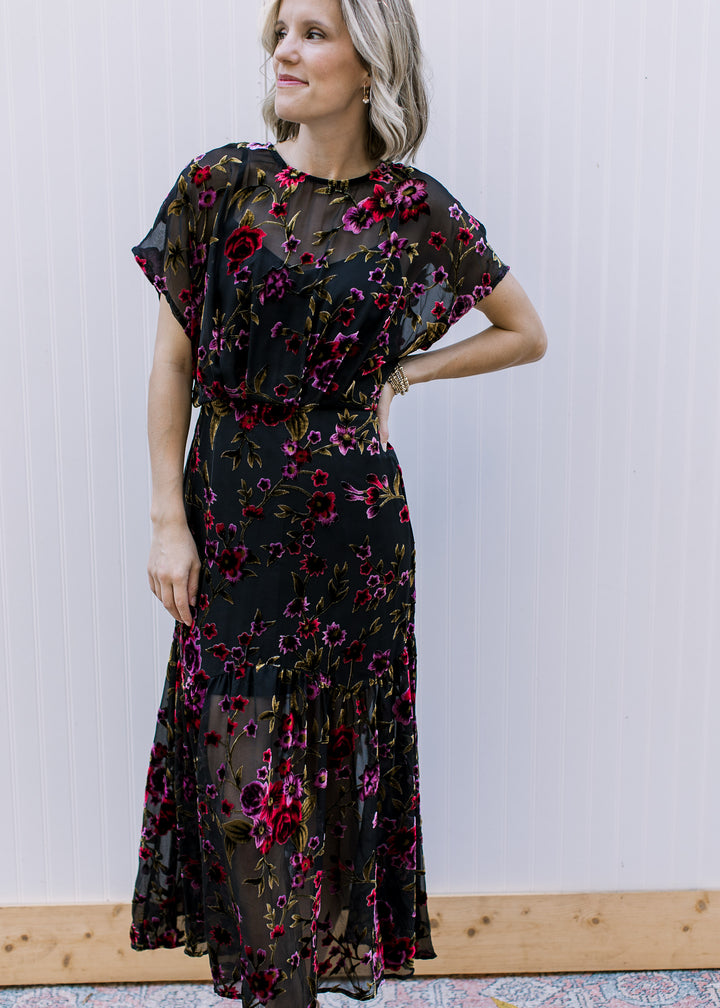 Model wearing a black midi with sheer overlay with velvet floral, attached slip and short sleeves.