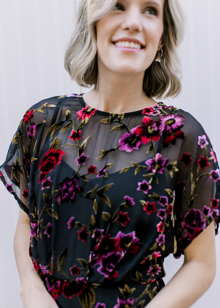 Close up of purple and pink velvet flowers on the sheer overlay of a midi short sleeve dress. 