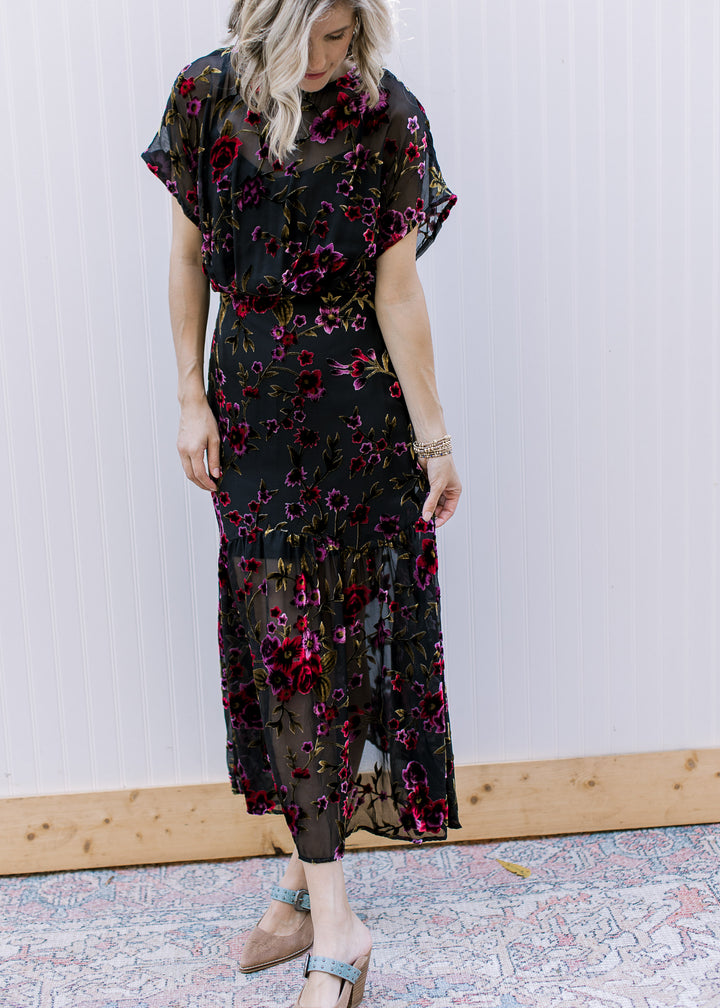Model wearing heels and a black midi with sheer velvet floral overlay, slip and short sleeves.