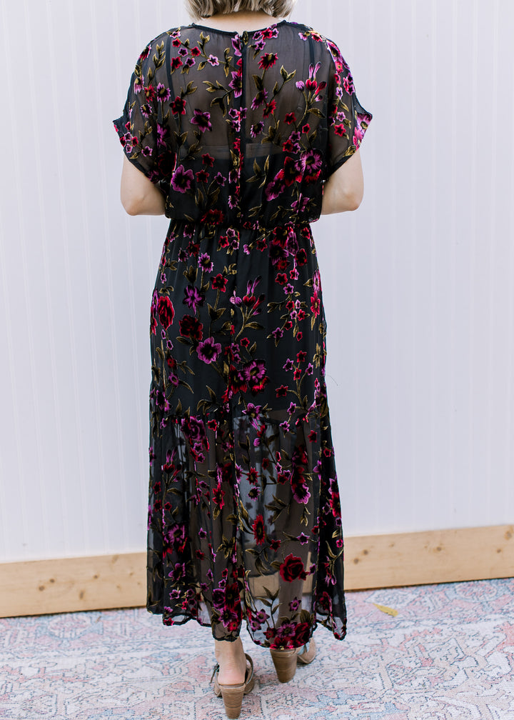 Back view of Model wearing a black midi with sheer floral overlay, hidden zip and short sleeves.