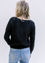 Back view of Model wearing a lightweight black ribbed top with long sleeves and a round neckline. 