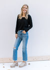 Model wearing jeans and a lightweight black ribbed top with long sleeves and a round neckline. 