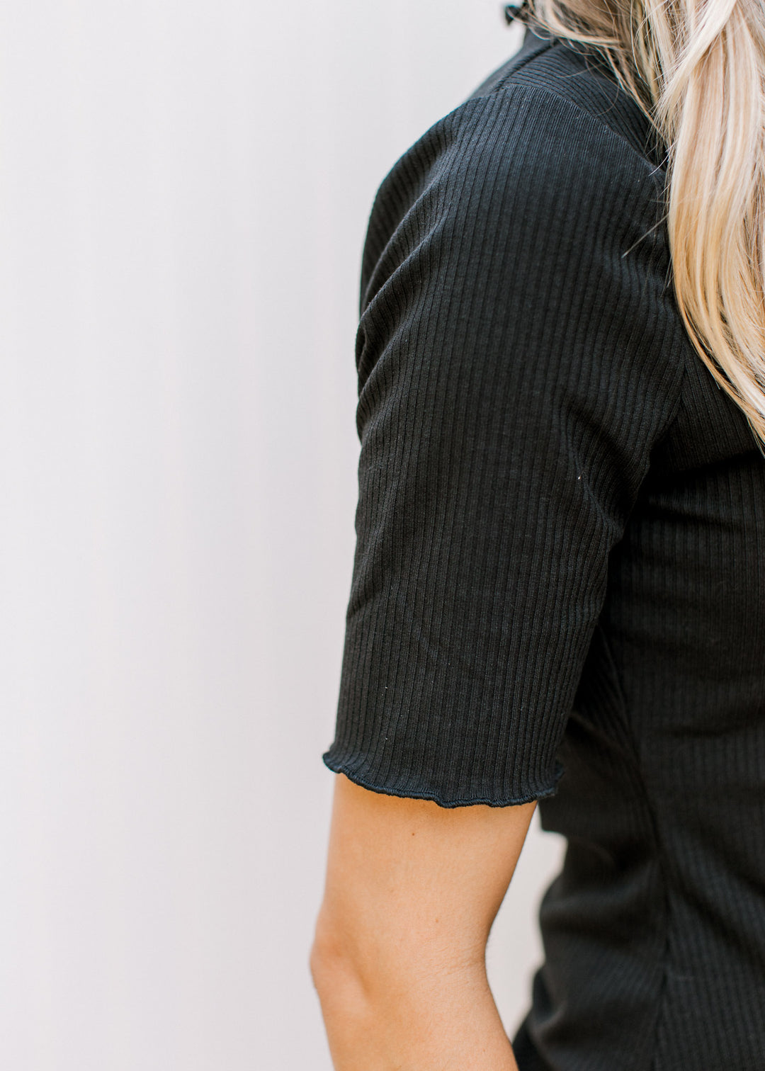 Close up of ruffled hem on the short sleeve of a ribbed back top with a mock neck.