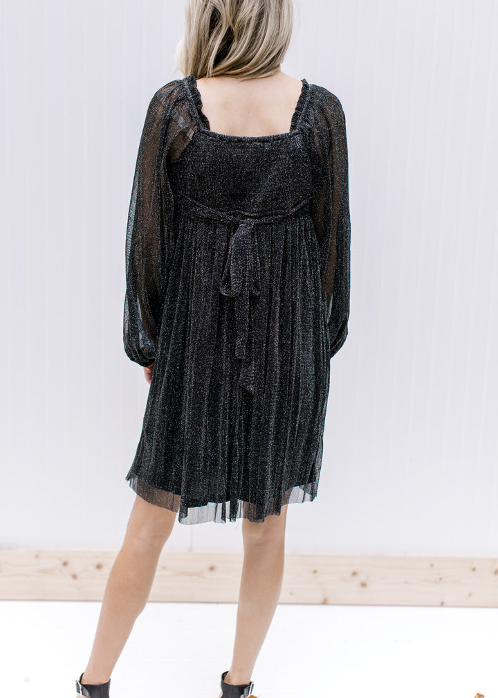 Back view of square neck and smocked back with a tie on a black shimmer above the knee dress. 
