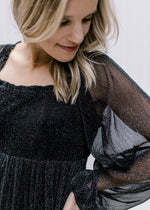 Close up of square neck and sheer long sleeves with elastic band on a black shimmery dress. 