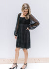 Model in heels and black shimmery above the knee dress with sheer long sleeves and a smocked back. 