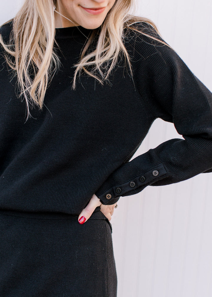 Model wearing a black ribbed set with a long sleeve top and round neck  with matching midi skirt. 