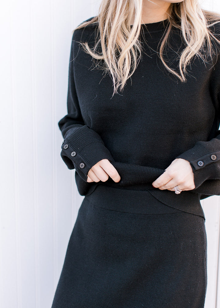 Close up of elastic band on a black midi skirt with matching long sleeve top with button at cuff. 