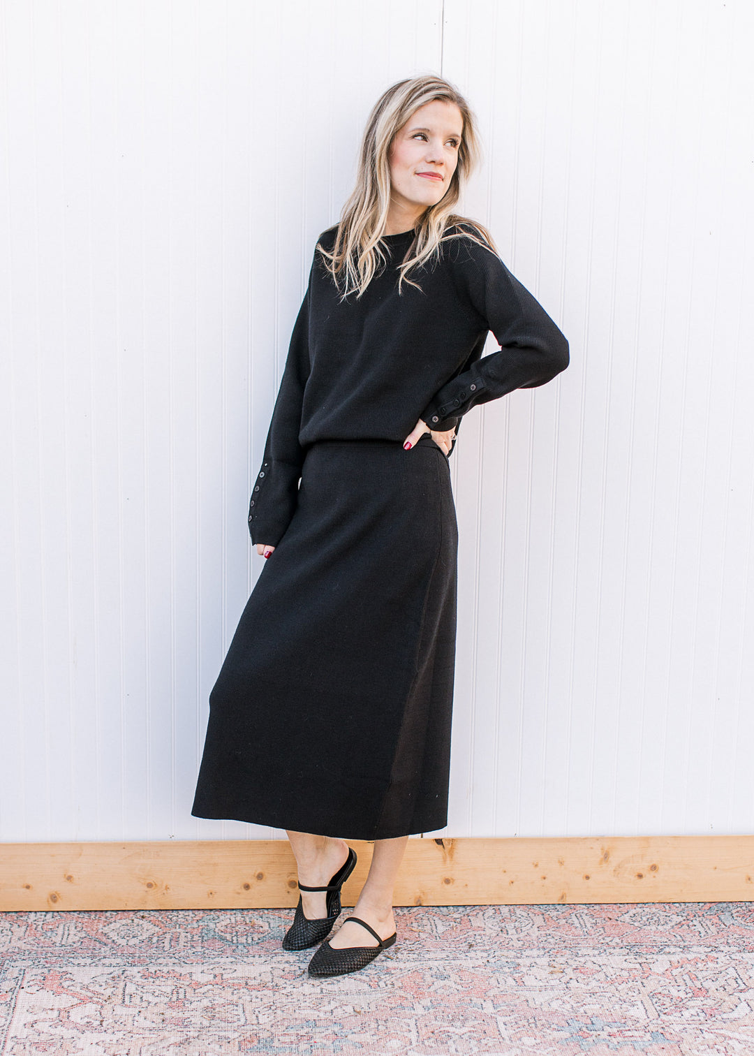 Model wearing flats and a black ribbed set with a long sleeve top and matching midi skirt. 