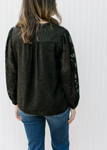 Back view of Model wearing a black top with textured flower pattern and long sheer sleeves. 