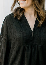 Close up of V-neck with pleating yolk and hidden button closure on a black long sleeve top.