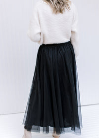 Back view of Model wearing a black tulle maxi skirt with an elastic waist with a sheer overlay.