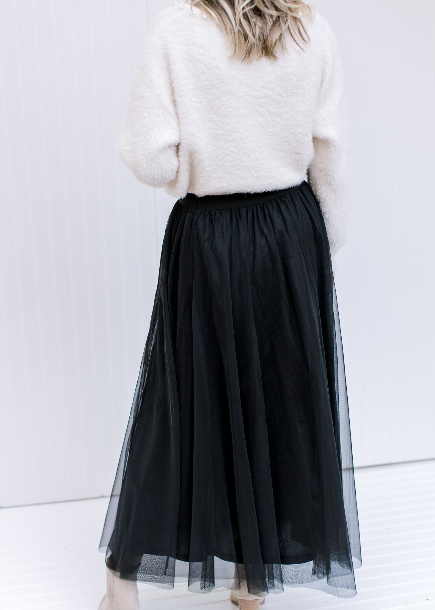 Back view of Model wearing a black tulle maxi skirt with an elastic waist with a sheer overlay.
