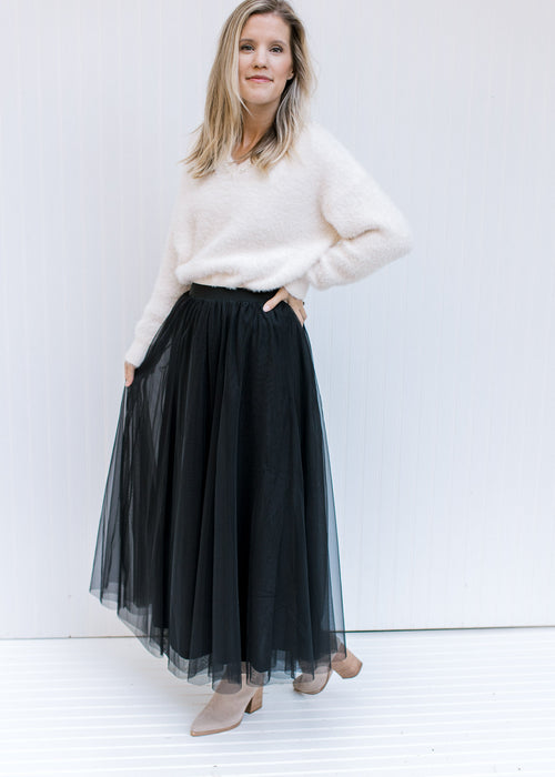 Model wearing a white top with a black tulle maxi skirt with an elastic waist with a sheer overlay.