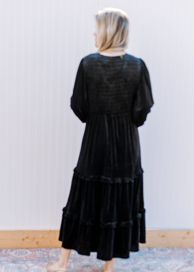 Back view of Model wearing a black velvet dress with bubble long sleeves, v-neck and tiered skirt.