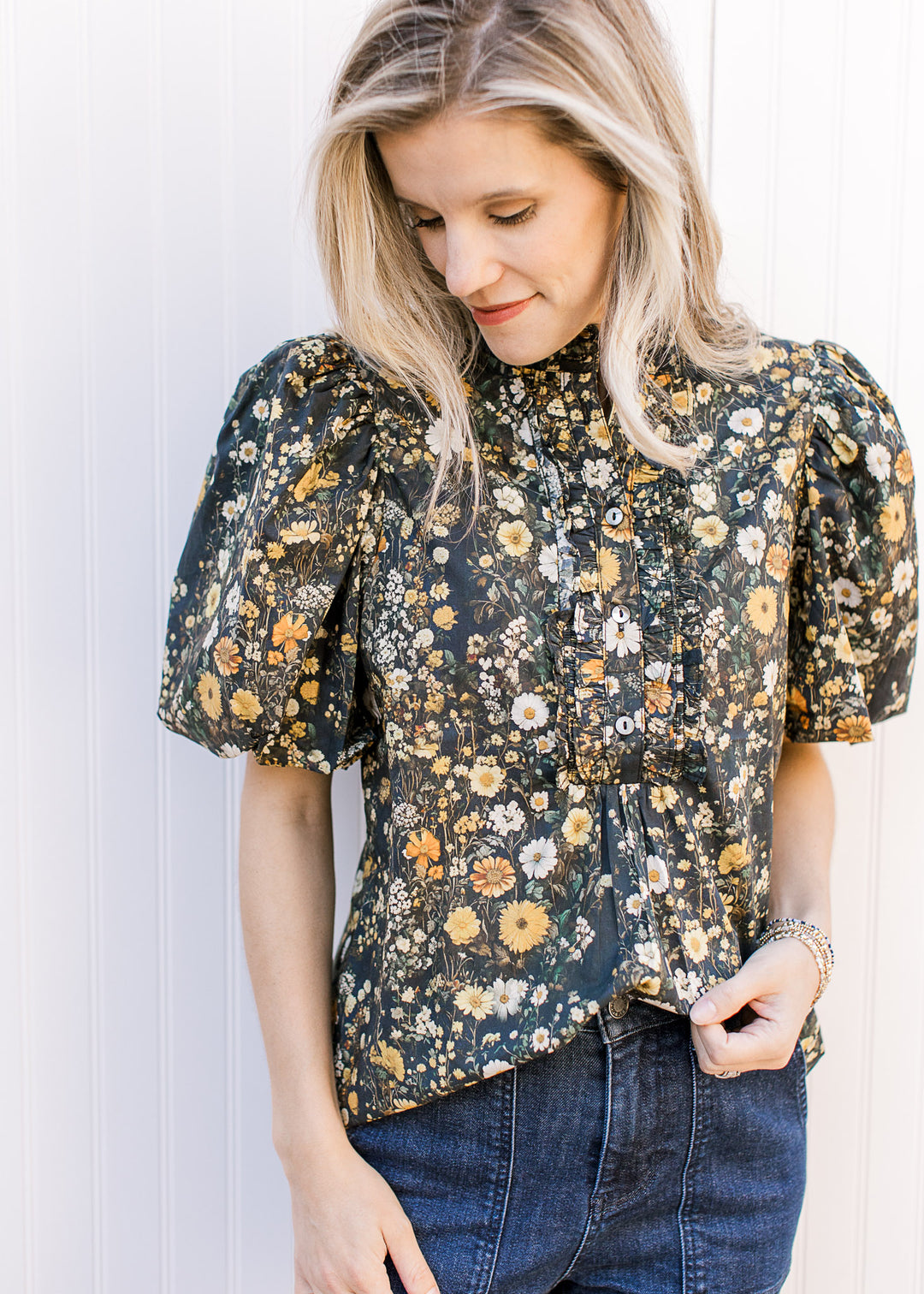 Model wearing a black top with soft floral, buttons, bubble short sleeves and ruffle neck.