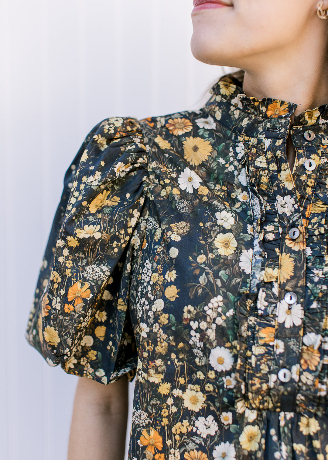 Close up of ruffle mock and bubble short sleeves with pleated shoulders on a black top with floral.