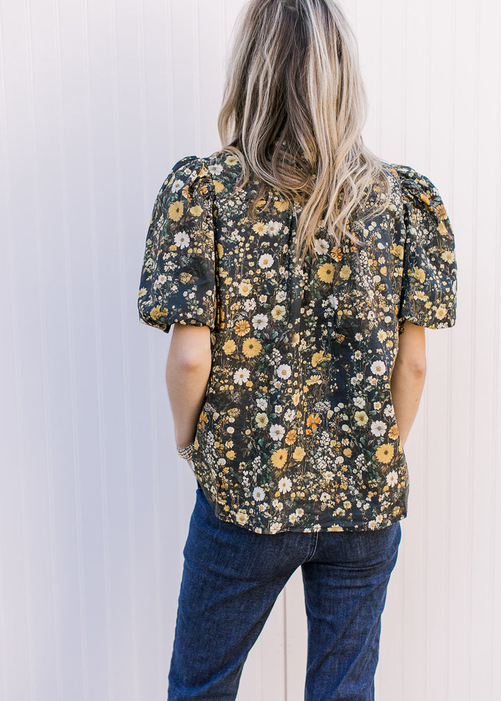 Back view of Model wearing a black top with floral, button front and bubble short sleeves.