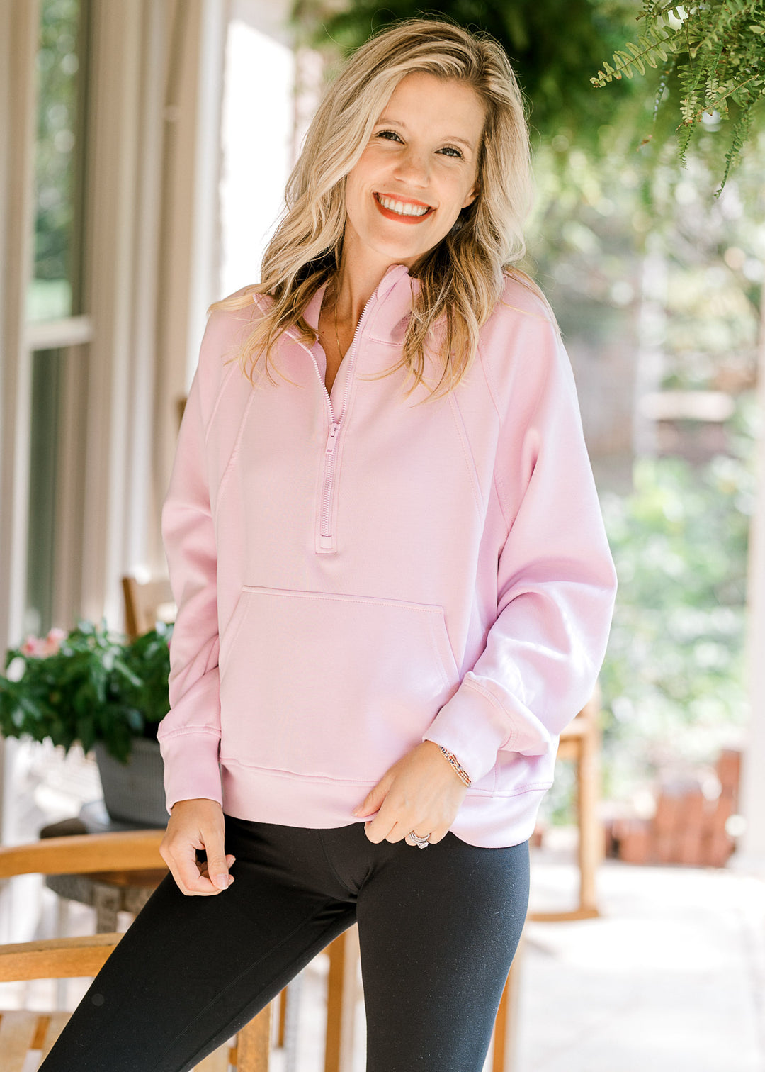 Model wearing black leggings and a light pink long sleeve pullover with a quarter-zip neck. 