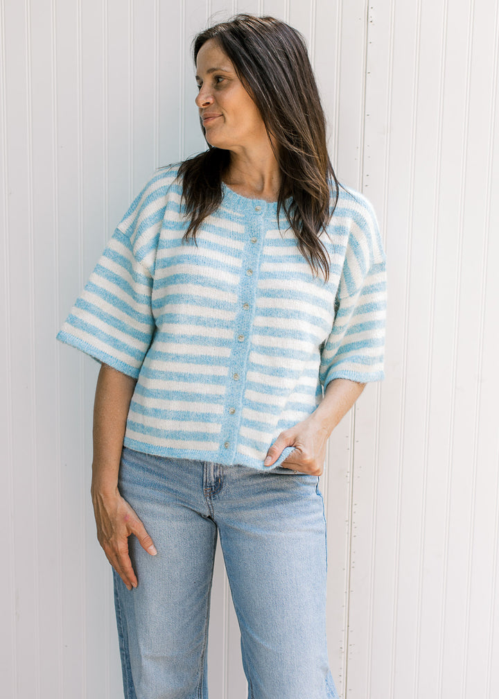 Model wearing jeans and baby blue and cream striped cardigan with buttons and elbow-length sleeves.