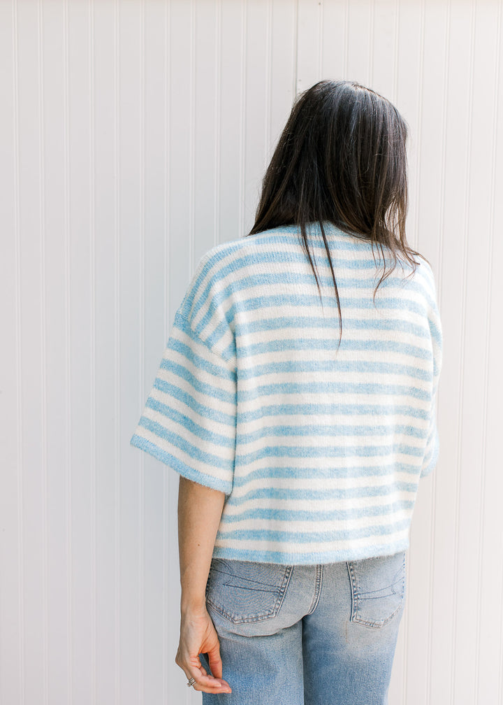 Back view of Model wearing a baby blue and cream striped cardigan with elbow-length sleeves.